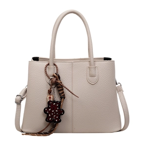 Elegant beige tote bag with litchi texture leather and leopard bear charm on white background