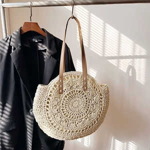 Chic beige round straw woven shoulder bag with brown leather handles in natural sunlight