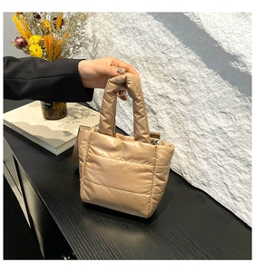 Detail of champagne gold quilted puffer handbag on a minimalist stone texture background