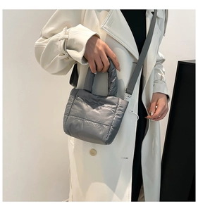 Close-up of grey quilted puffer bag with crossbody strap on a white trench coat
