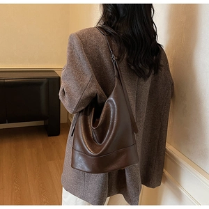 Detail view of a large dark brown bucket bag in shiny vintage leather on a model's shoulder