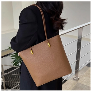 Sac fourre-tout en cuir marron avec détails dorés sur un modèle en costume noir chic
