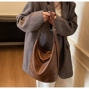 Detail of dark brown leather bucket bag with wide shoulder strap and silver buckle
