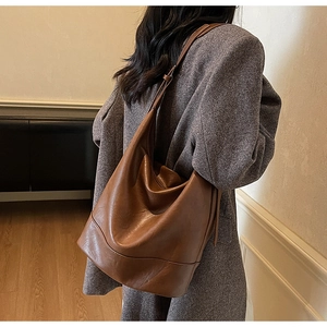 Rear view of model wearing a large brown vintage leather bucket bag with wide strap