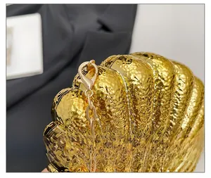 Détail du sac coquille doré avec texture en métal martelé et fermoir à chaîne