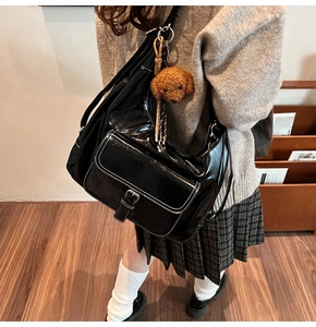 Detail of black glossy shoulder bag with white contrast stitching and plush dog charm