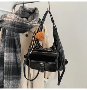 Detail of black glossy patent leather backpack with white stitching and teddy bear charm
