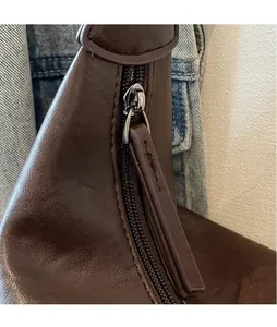 Detail of a brown leather bucket bag showing an elongated zipper pull and metal hardware