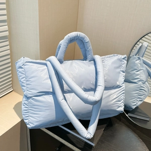 Quilted light blue puffer tote bag with padded handles and long strap in modern setting