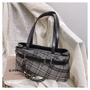 Detail of grey plaid Boston bag with leather handles and decorative woven pendant