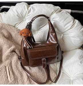 Deep brown oil-wax crescent bag with contrast stitching and plush dog charm accessory