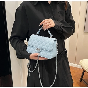 Detail view of light blue quilted leather bag with turn-lock and woven chain strap