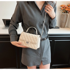 Detail of a beige quilted crossbody bag with a metal twist-lock and woven chain strap