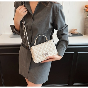 Detail of white quilted crossbody bag with silver clasp and metal chain on a model