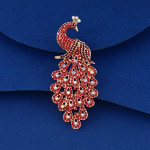 Détail de la broche paon avec strass rouges et base dorée sur fond bleu texturé