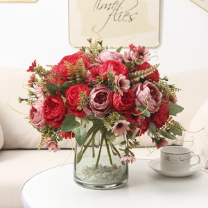 Realistic red and pink faux peonies in a glass vase with stones for home decoration