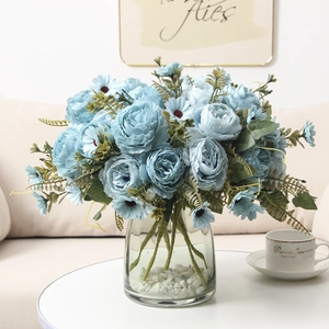 Blue artificial roses and daisies in glass vase with stones for home decoration