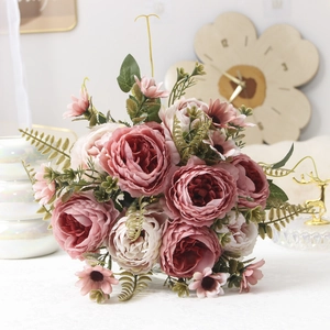 Close-up of pink and cream faux peonies with green leaves in a home decor setting