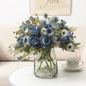 Blue peonies and white daisies in a glass vase with pebbles on a white table