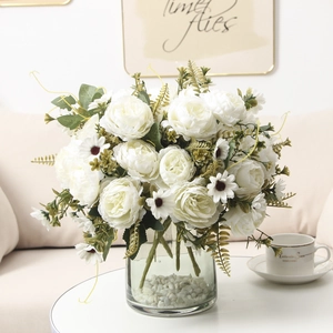 Close-up of white artificial peonies and daisies in a glass vase with white pebbles