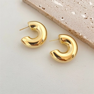 Macro shot of polished gold-plated C-shape chunky drop earrings on white textured stone