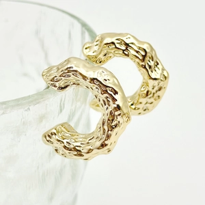 Detail of chunky gold-plated C-shaped earrings with unique molten lava textured finish