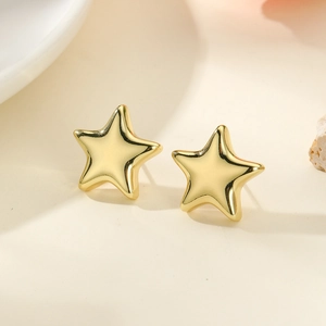 Detailed close-up of polished gold star earrings on a minimalist cream aesthetic surface