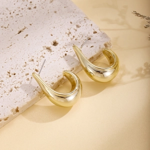 Macro shot of gold teardrop earrings with mirror polish finish on white textured stone