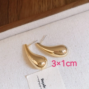 Macro shot of gold teardrop earrings measuring 3x1cm on a textured linen background