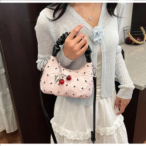 Detail of pink hobo bag with ruffle strap and cherry charm shown on light blue cardigan