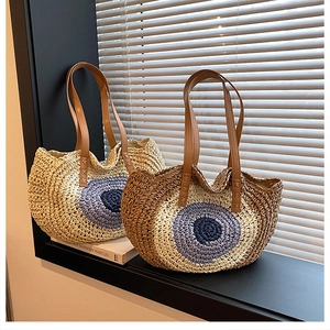 Detail of round straw shoulder bag with evil eye pattern and brown leather handle