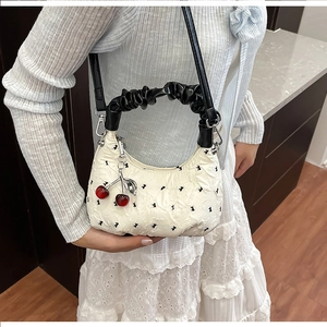 Close-up of pleated white bag with black bow print and cherry charm detail