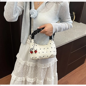 Detail of white pleated crescent bag with black bow patterns and cherry charm