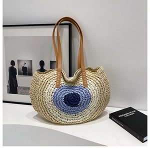 Close-up of woven straw shoulder bag with blue eye pattern and leather handle details
