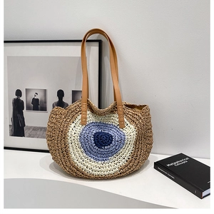 Close-up of woven straw bag with Evil Eye pattern and reinforced brown leather handles