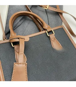 Detail of black lychee grain and brown leather stitching on a fashion tote bag