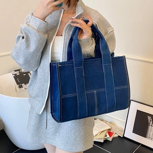 Detail of dark blue denim tote bag with white contrast stitching and reinforced handles