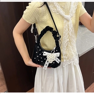 Detail of black glossy handbag featuring lace bow, pearl heart and sparkly rhinestones