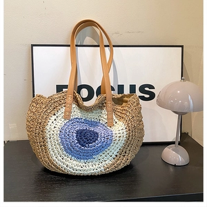 Detail of woven straw shoulder bag with blue eye pattern and leather handles