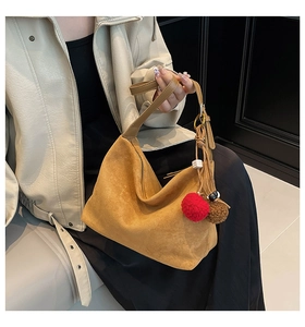Close-up of yellow suede hobo bag featuring a decorative plush charm and smooth zipper