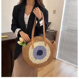 Close-up of circular woven beach bag featuring a blue evil eye pattern and leather straps
