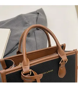 Detailed close-up of textured black and brown leather tote bag with gold lettering