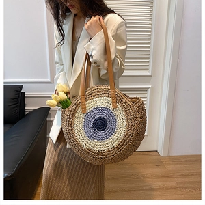 Detail of bohemian round straw bag with blue concentric patterns and leather handles
