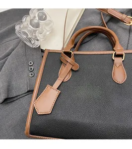 Detail of black litchi grain leather bag with brown trim and golden round hardware