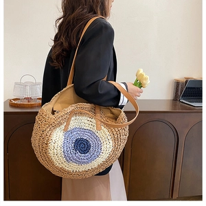 Detail of round straw shoulder bag featuring blue evil eye pattern and leather strap