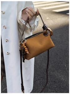 Close-up of brown suede Boston bag with gold ring buckle and beaded tassel detail