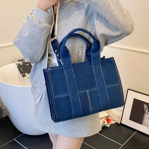 Detail of a deep blue denim tote bag featuring white contrast stitching and a wide canvas strap