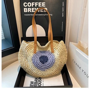 Detail of woven straw shoulder bag with evil eye motif and brown leather strap