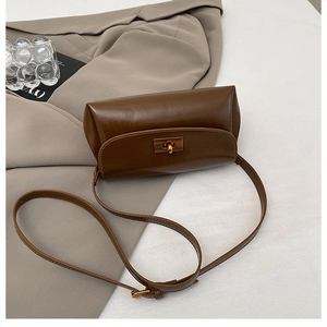 Detail of vintage brown leather crossbody bag with gold textured metal twist lock on a blazer