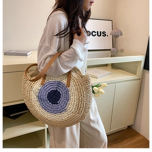 Macro detail of hand-woven straw shoulder bag with evil eye pattern and leather handle